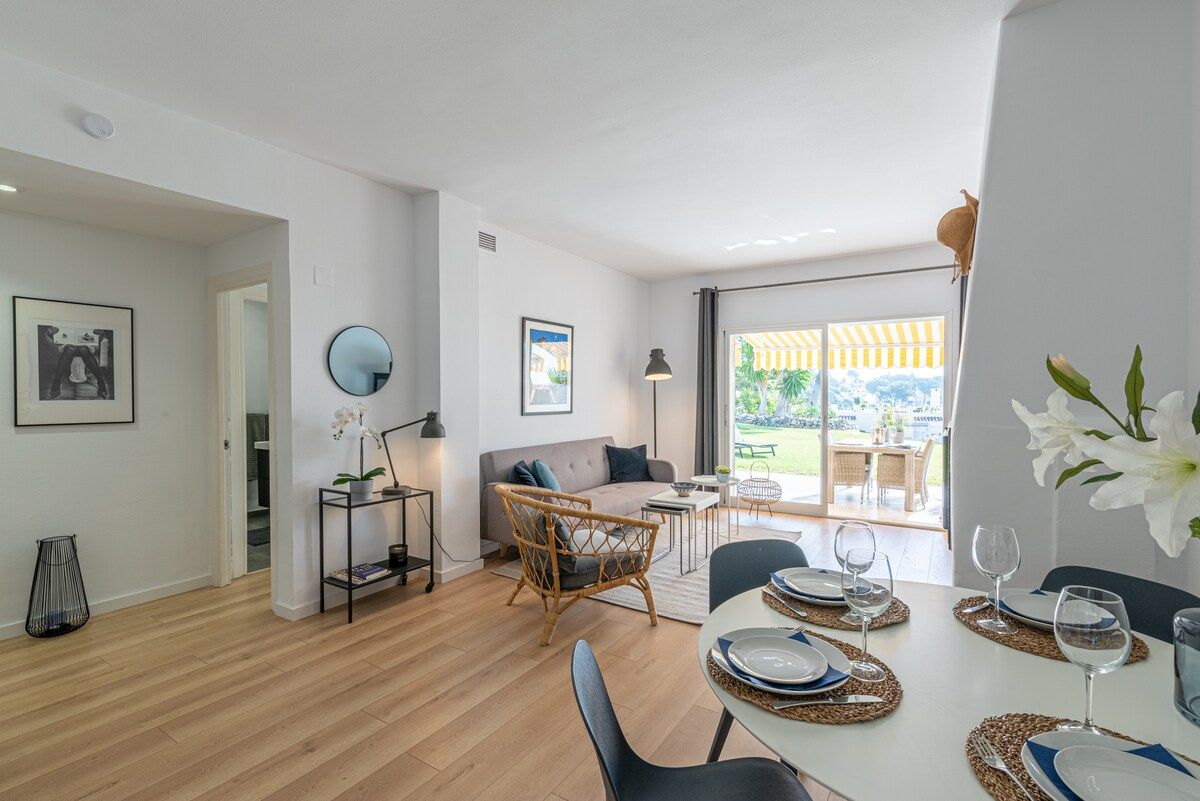 Un salon moderne avec un canapé, une table à manger pour deux personnes et une vue sur l’extérieur.