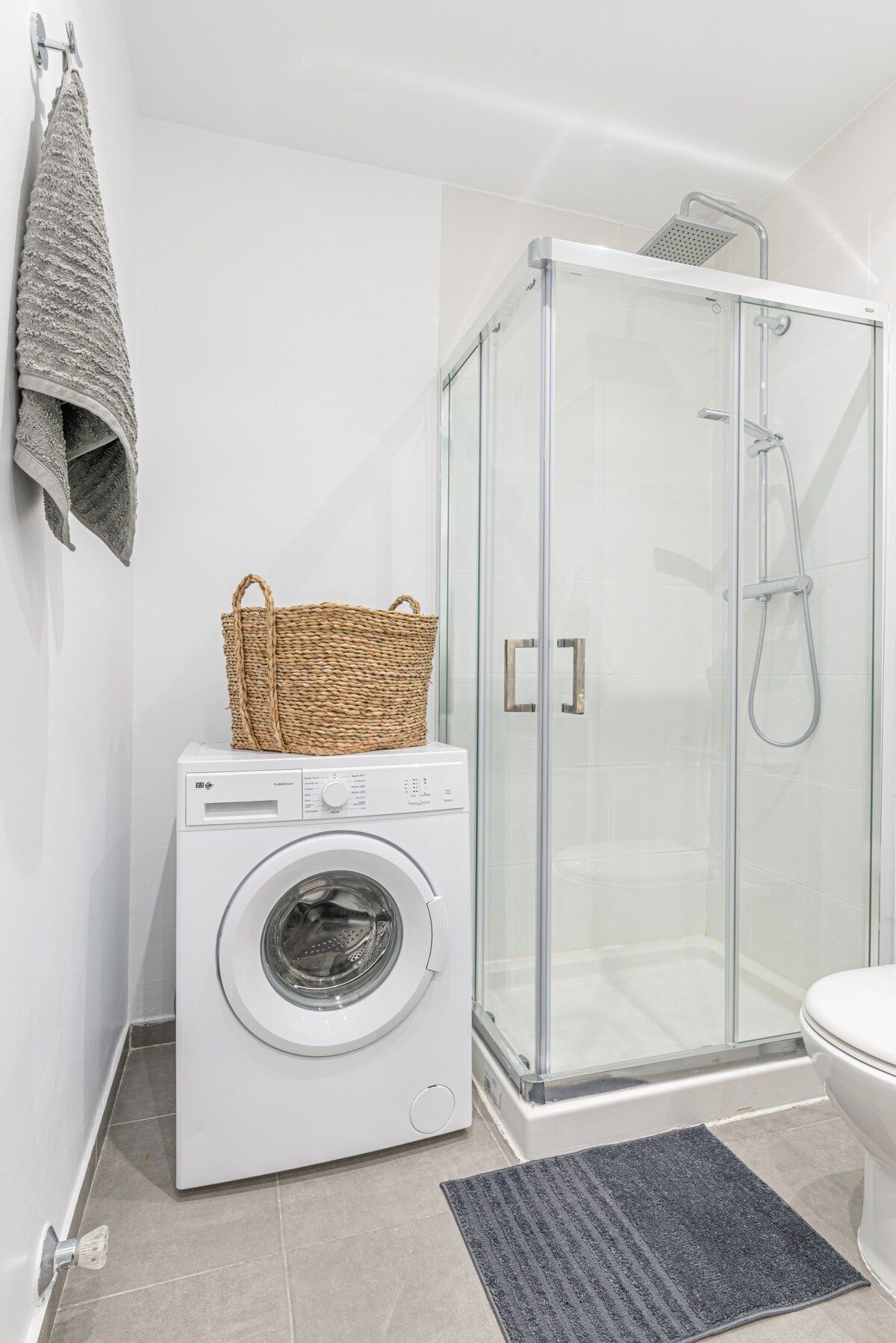 Une petite salle de bain équipée d’un lave-linge, d’une douche à parois de verre et d’un porte-serviettes.