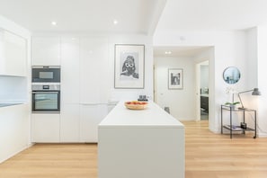 Una cucina moderna con mobili bianchi, un'isola centrale e un'opera d'arte incorniciata appesa al muro.