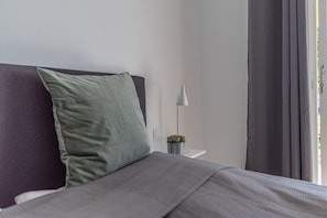 Un letto con una coperta grigia, un cuscino verde e una piccola pianta in vaso su un comodino.