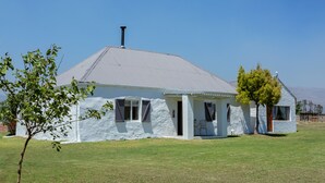 Uma casa térrea com telhado inclinado e chaminé, rodeada por um gramado e algumas árvores.