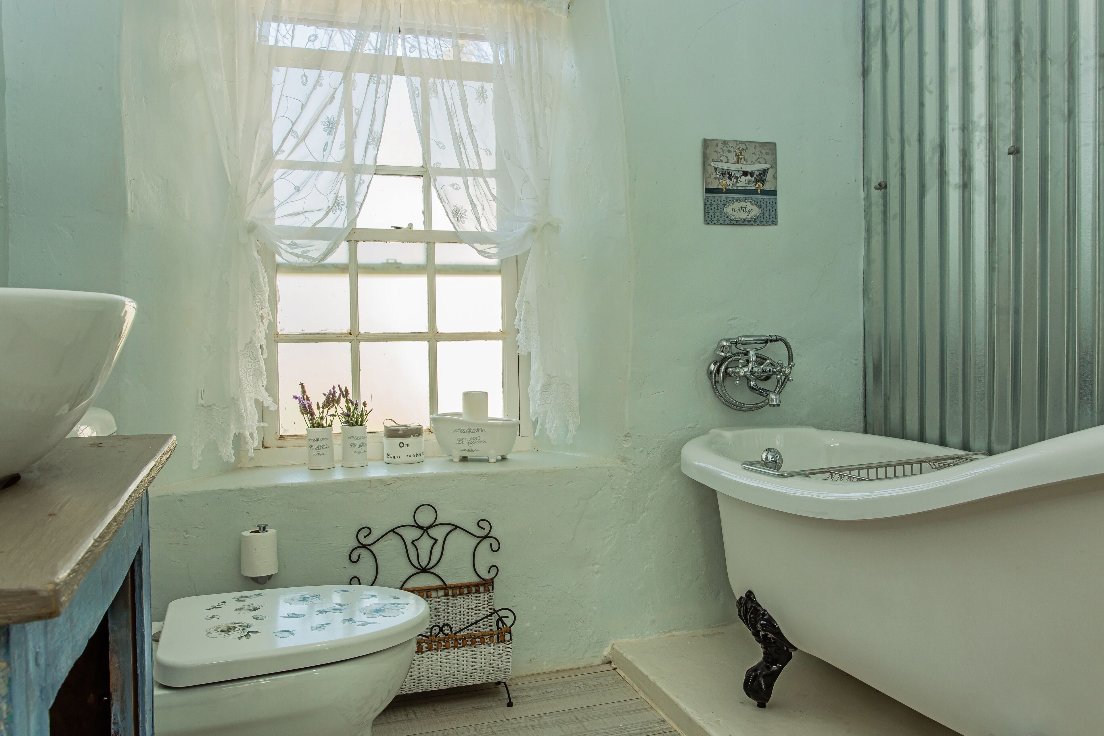 A bathroom with a white bathtub, a toilet, and a window with lace curtains.
