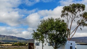 Um edifício branco com uma árvore à frente, uma montanha ao fundo e um céu claro.