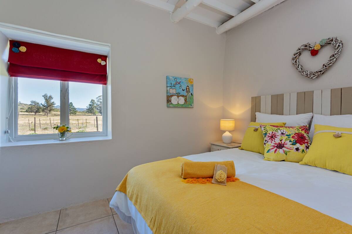 Een slaapkamer met een bed, een raam met rood gordijn, een wanddecoratie en een bedlampje.