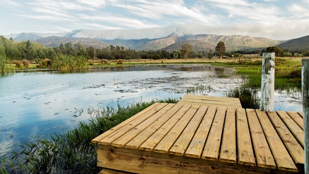 Une jetée en bois s’étendant au-dessus d’une étendue d’eau calme, avec en arrière-plan des montagnes et un ciel dégagé.