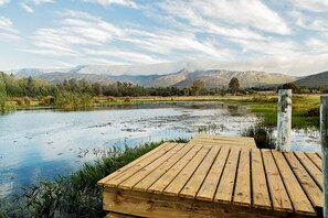Eine Holzstege, der sich über ruhiges Wasser erstreckt, mit Bergen und klarem Himmel im Hintergrund.