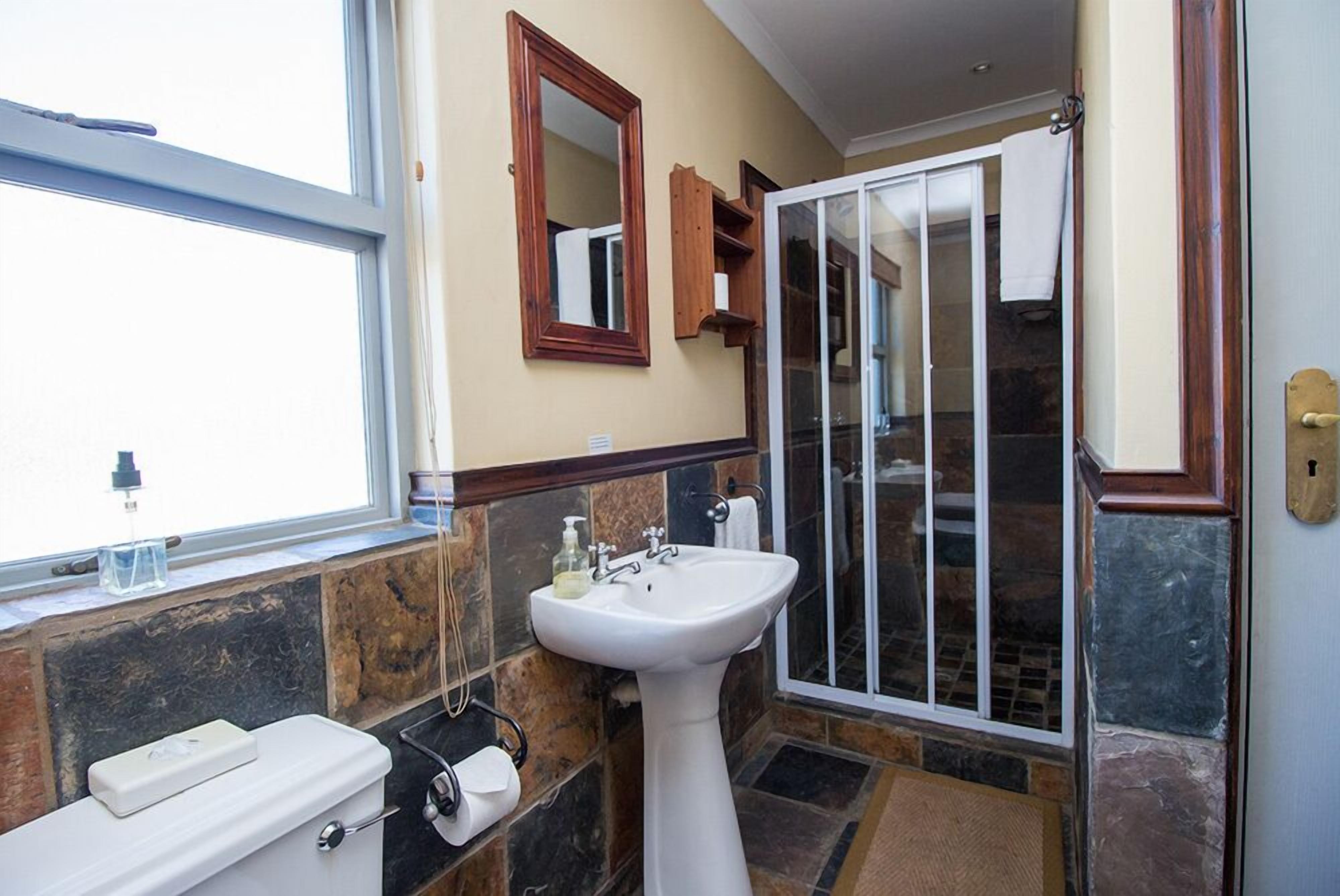 Un baño con inodoro, lavamanos, espejo y zona de ducha.