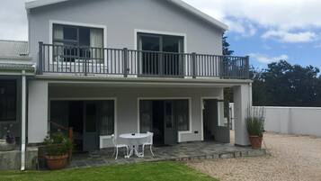 A two-story house with a balcony, a covered patio with a table and chairs, and a well-maintained lawn.