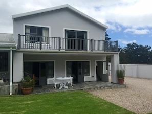 A two-story house with a balcony, a covered patio with a table and chairs, and a well-maintained lawn.
