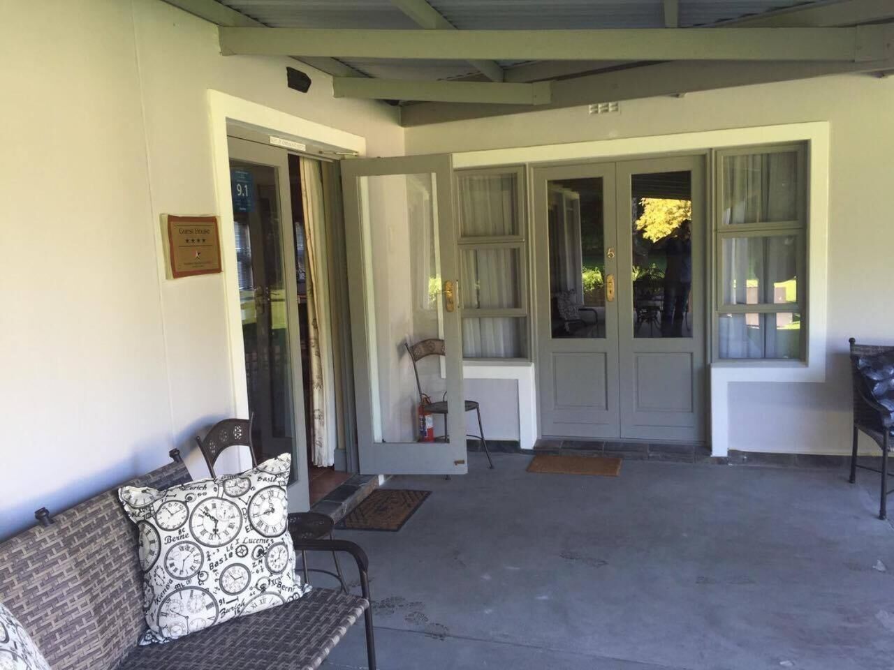 A covered porch with a bench, a door leading to a room, and a window with curtains.