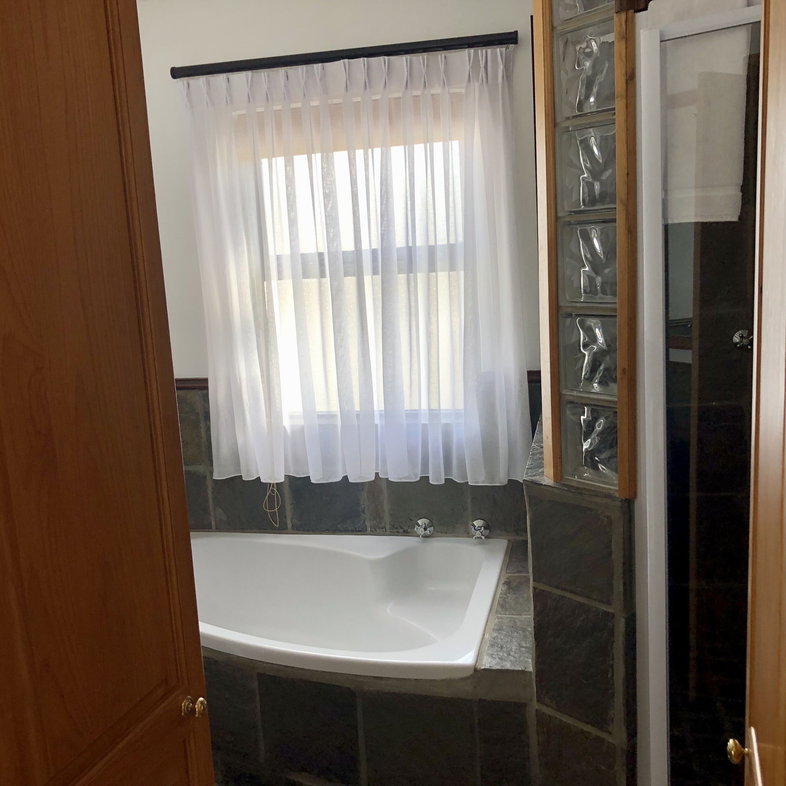 Une salle de bain avec une baignoire, une fenêtre avec des rideaux légers et un espace douche doté de portes en verre.