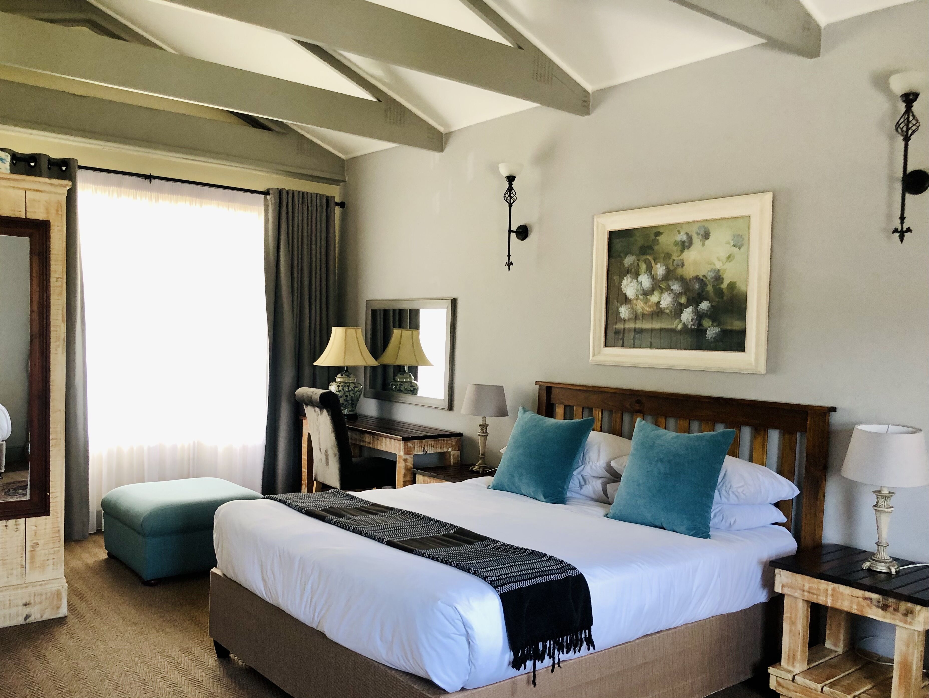 Habitación de hotel con una cama grande, un escritorio con lámpara, una silla, un armario y un cuadro en la pared.