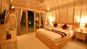 A spacious bedroom with a large bed, wooden headboard, and a sliding glass door leading to a balcony. - Kompyang Cottage (Penida Island)