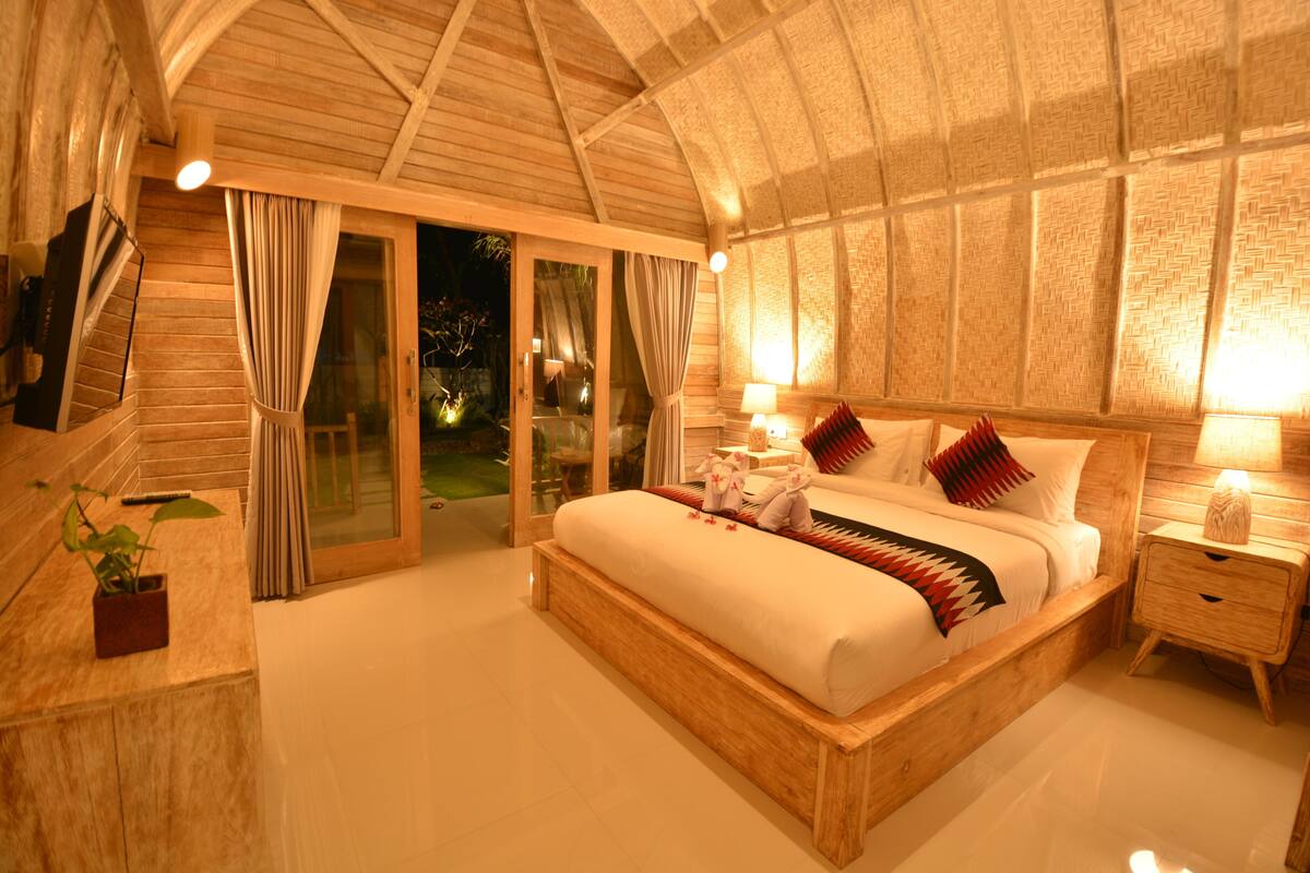 A spacious bedroom with a large bed, wooden headboard, and a sliding glass door leading to a balcony.