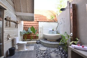 A compact bathroom with a toilet, sink, and bathtub. There are plants and a small garden area.