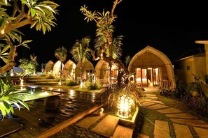 A nighttime view of a resort with overwater bungalows, a swimming pool, and well-lit pathways. - Kompyang Cottage (Penida Island)