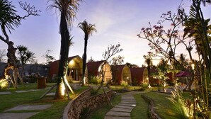 A well-maintained garden with a stone pathway leading to a building with multiple arched windows. - Kompyang Cottage (Penida Island)