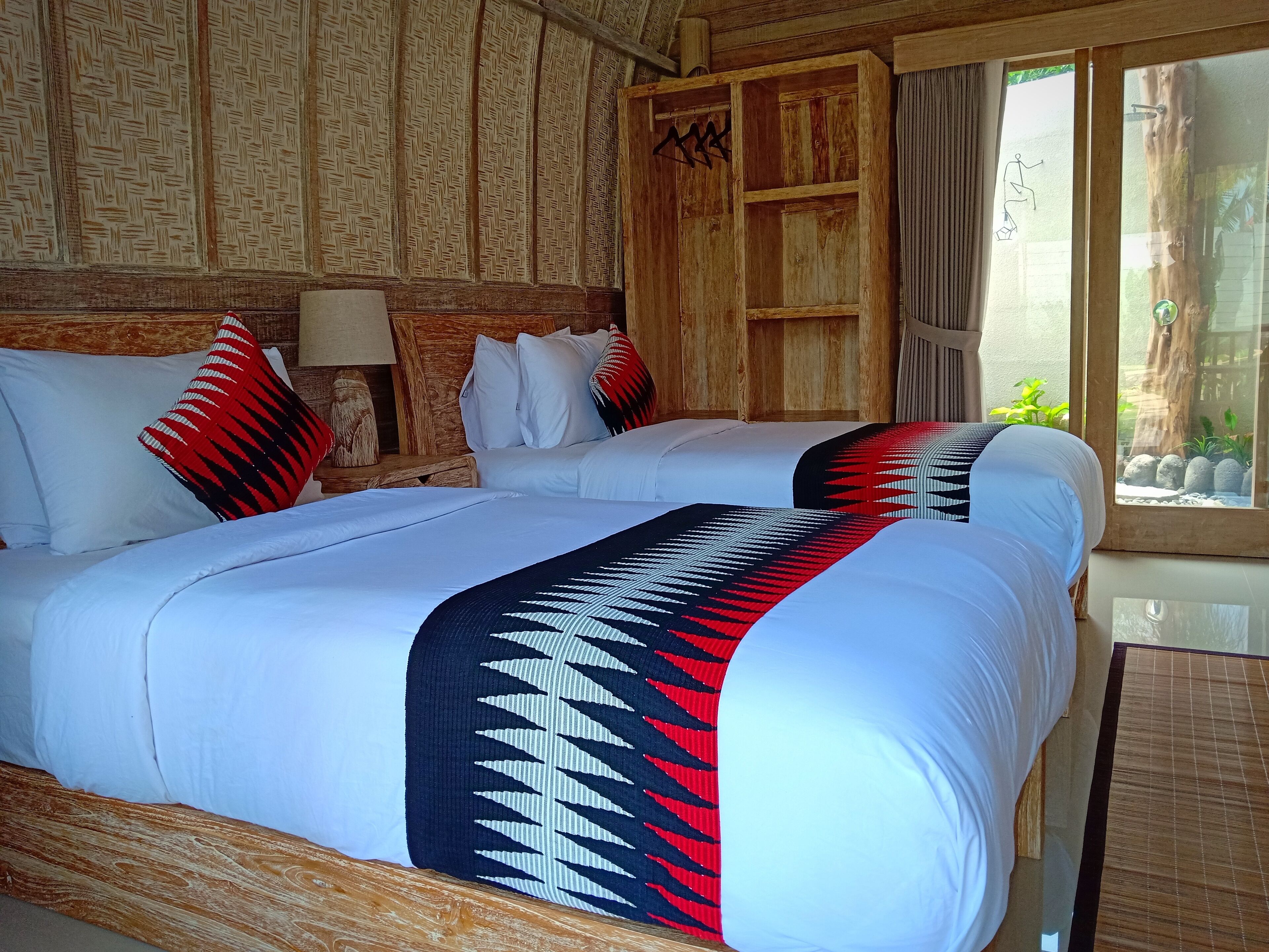 A room with a large bed, wooden headboard, and a window with a view of rocks and greenery.