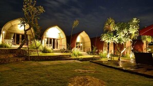 Two dome-shaped buildings with a well-maintained lawn and palm trees. - Kompyang Cottage (Penida Island)