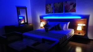 Ein modernes Hotelzimmer mit Bett, Nachttischlampen, einem Nachttisch, einem Schreibtisch und einem Sessel.