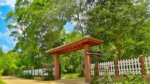 Ein Gartenportal mit einer Holzpergola, einem weißen Zäunchen und einem Schild mit der Aufschrift 'Heaven In Satinwoods'.