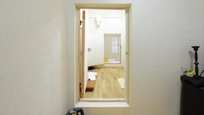 En smal dörröppning leder in till ett rum med trägolv, en säng och ett litet bord med en lampa.