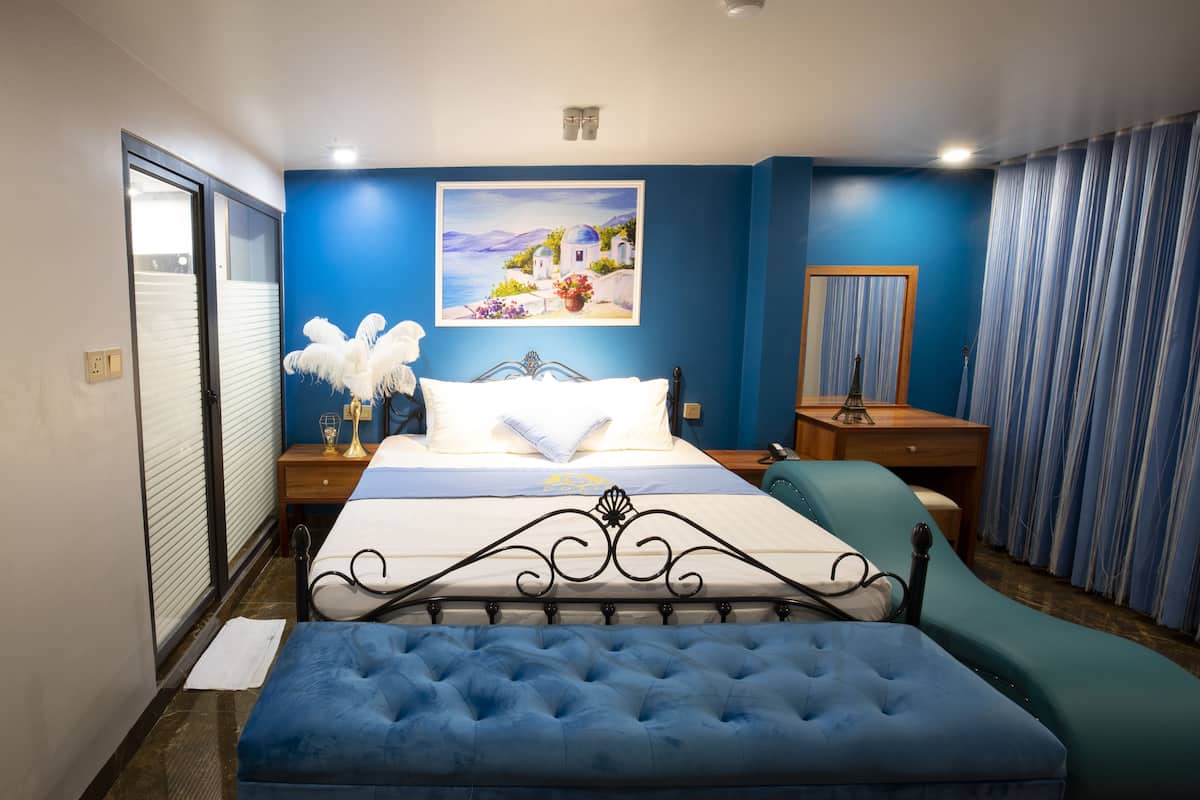 A bedroom with a bed, a nightstand, a chair, a desk, a mirror, and a painting on the wall.