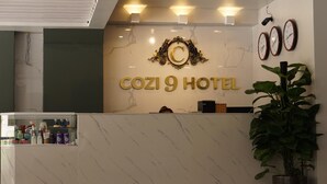 Un comptoir d’accueil à l’hôtel COZI 9, doté d’un dessus en marbre, d’une vitrine en verre contenant des articles de toilette et d’une grande enseigne décorative placée au-dessus du comptoir.