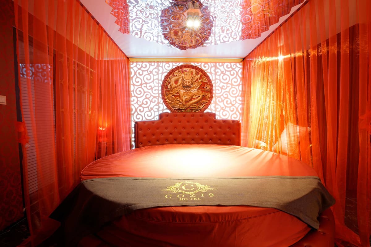 A hotel room with a tufted headboard, red curtains, and a decorative ceiling light fixture.