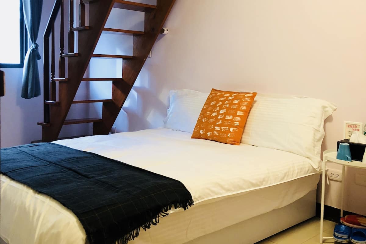 A bedroom with a bed, a wooden staircase, a nightstand, and a window with curtains.