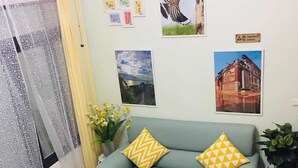 A living room with a sofa, a coffee table, and a small plant. There are pictures on the wall and a clock. - Yi Jia Homestay (Jinning)