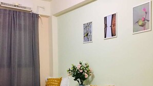 A hotel room with two beds, each with a blue blanket and a yellow pillow. There is a small table with a vase of flowers and a teddy bear on one bed. The walls are light green, and there are three framed pictures on the wall. - Yi Jia Homestay (Jinning)
