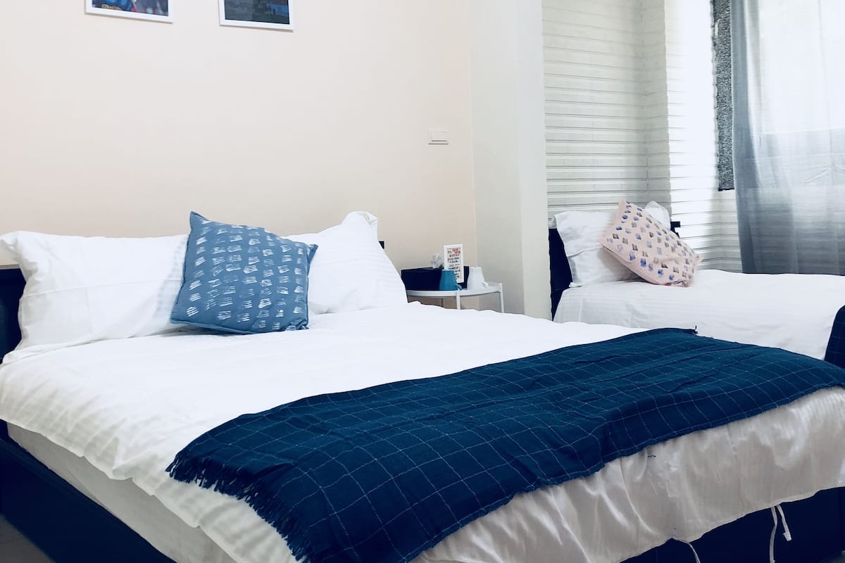 A hotel room with two beds, a window with curtains, and a wall-mounted air conditioner.