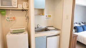 A compact hotel room with a microwave, a small sink, a mini fridge, and a bed with a blue and white patterned bedspread. - COCO Fukuoka Chiyo (Fukuoka)