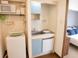A compact hotel room with a microwave, a small sink, a mini fridge, and a bed with a blue and white patterned bedspread.