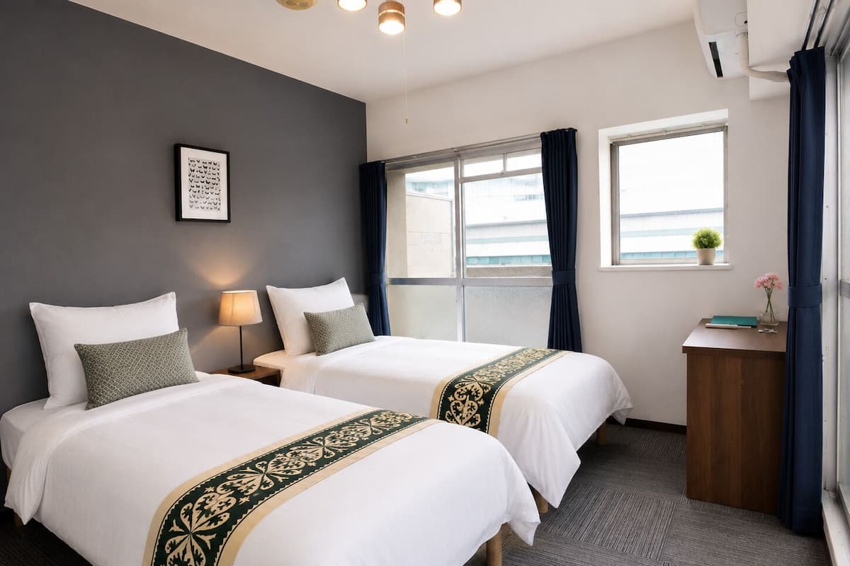 Una habitación de hotel con dos camas, un escritorio, una ventana con cortinas, un aire acondicionado instalado en la pared y un cuadro enmarcado.