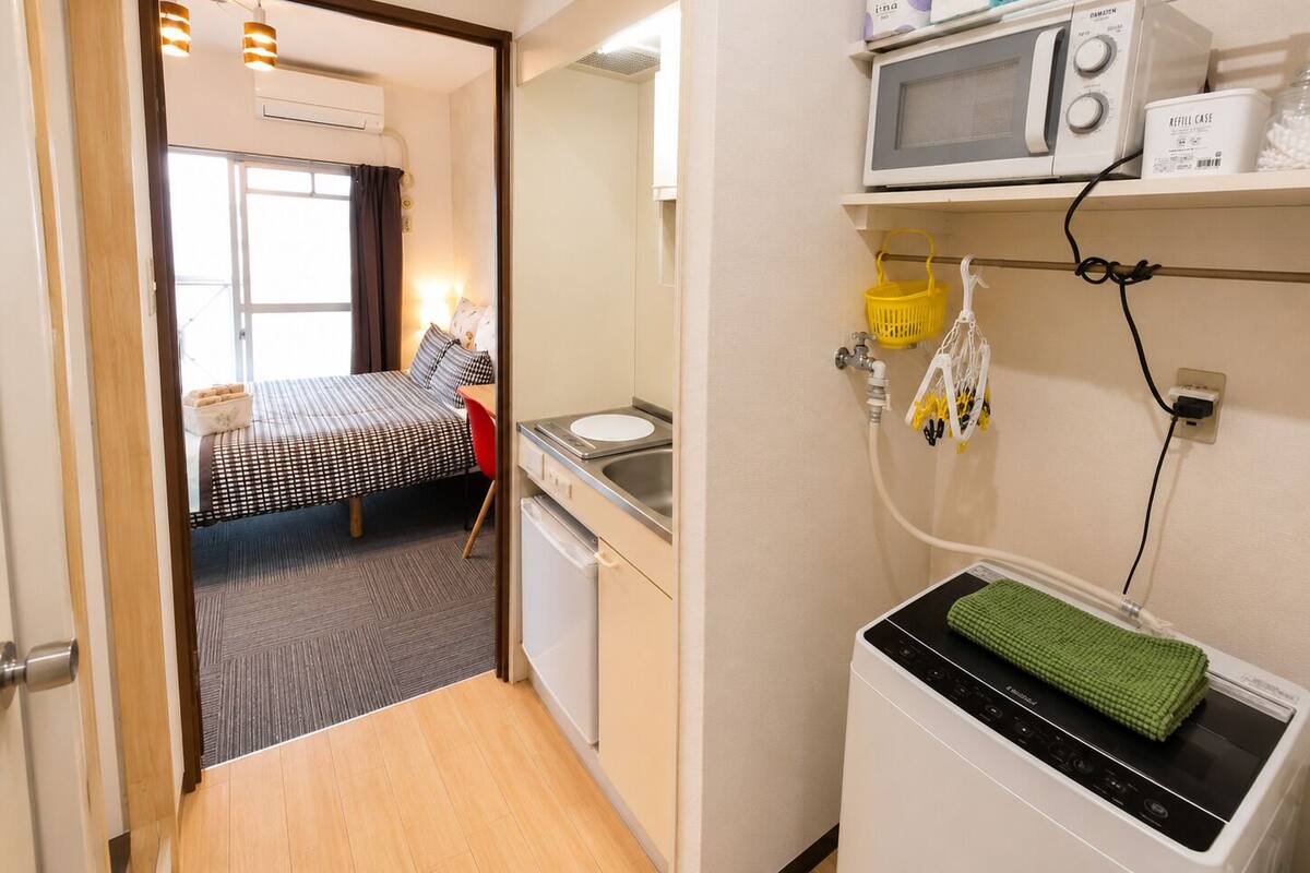 Habitación de hotel compacta con cama, pequeña cocina, microondas y lavadora.