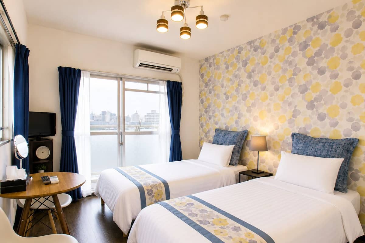 Habitación de hotel con dos camas, un escritorio, una silla, un televisor y una ventana con cortinas.