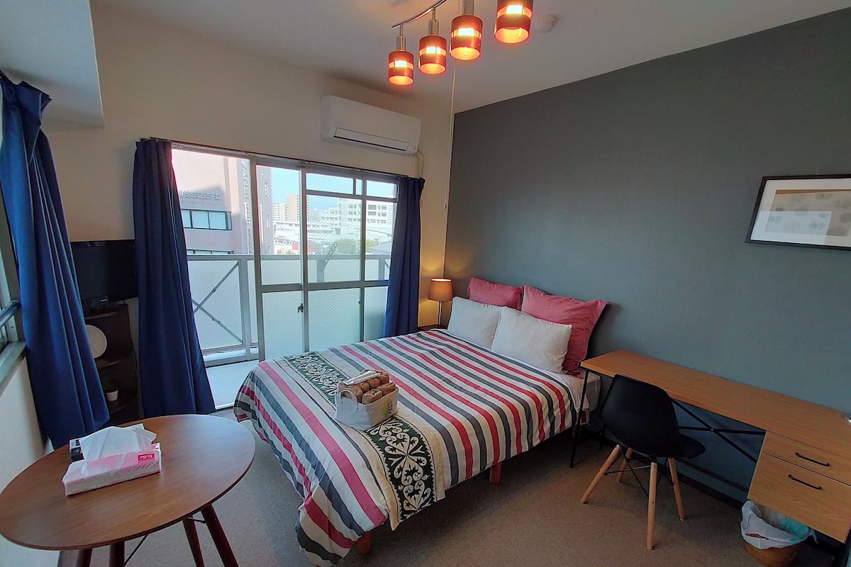 Habitación de hotel con cama, escritorio, silla, mesita y ventana con cortinas.