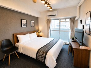 Ein Hotelzimmer mit Bett, Schreibtisch, Stuhl, Fernseher und einem Fenster mit Vorhängen.