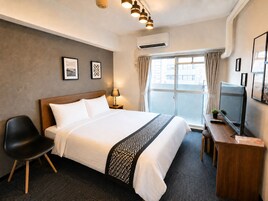 Una habitación de hotel con cama, escritorio, silla, televisor y ventana con cortinas.