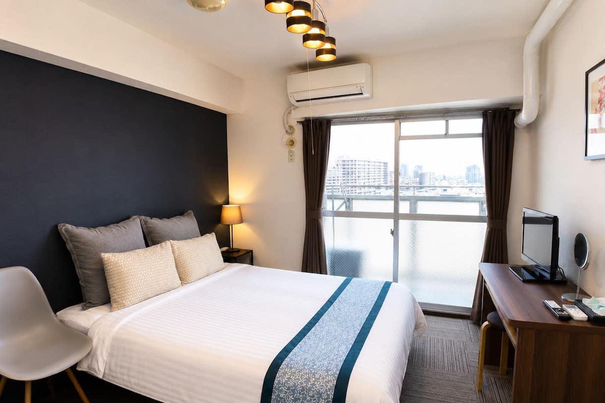 Habitación de hotel con cama, escritorio, silla y vista a la ciudad por la ventana.