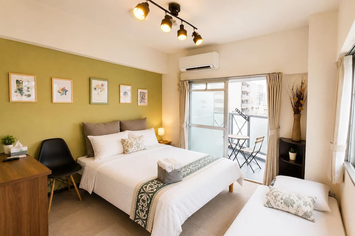 Habitación de hotel con dos camas, un escritorio, una silla, un balcón con mesa y sillas, y obras de arte en las paredes.