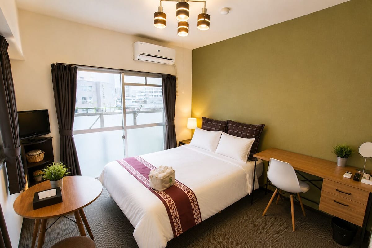 Habitación de hotel con cama, escritorio, silla, televisor y vista a la ciudad.