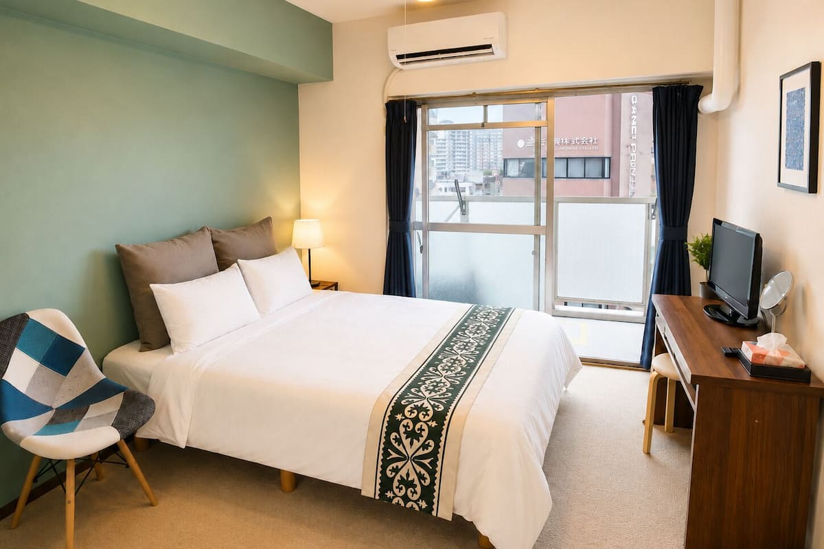 Una habitación de hotel con cama, escritorio con computadora, silla y ventana con cortinas.