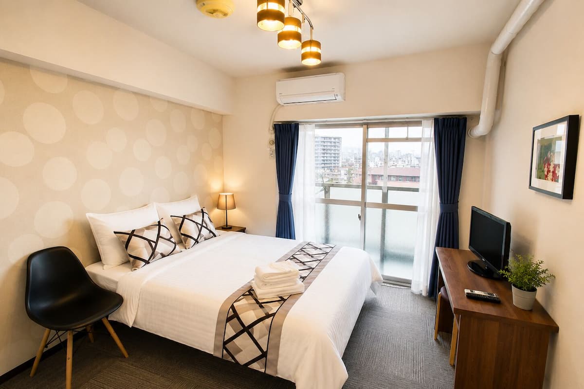 Habitación de hotel con cama, escritorio, silla, televisor y vista a la ciudad por la ventana.