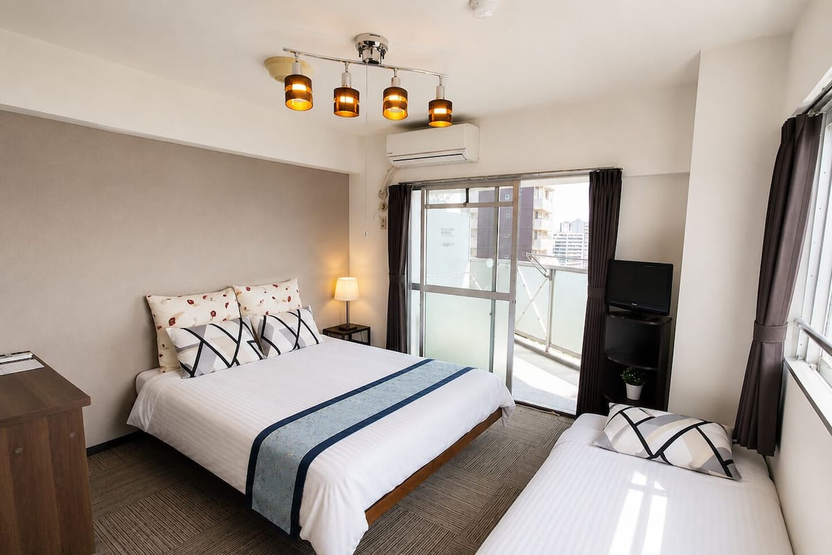 Habitación de hotel con cama, escritorio, televisor y balcón con vistas.