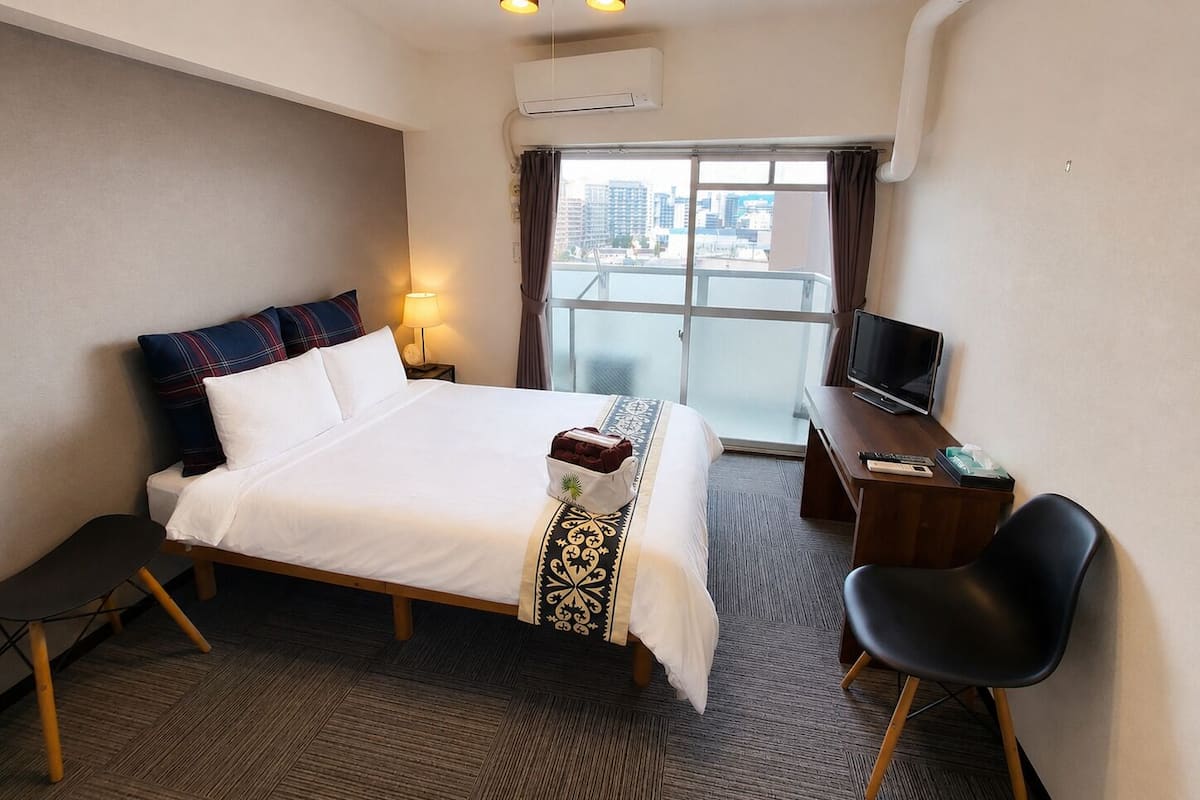 Una habitación de hotel con cama, escritorio con televisor, silla y ventana con vista a la ciudad.