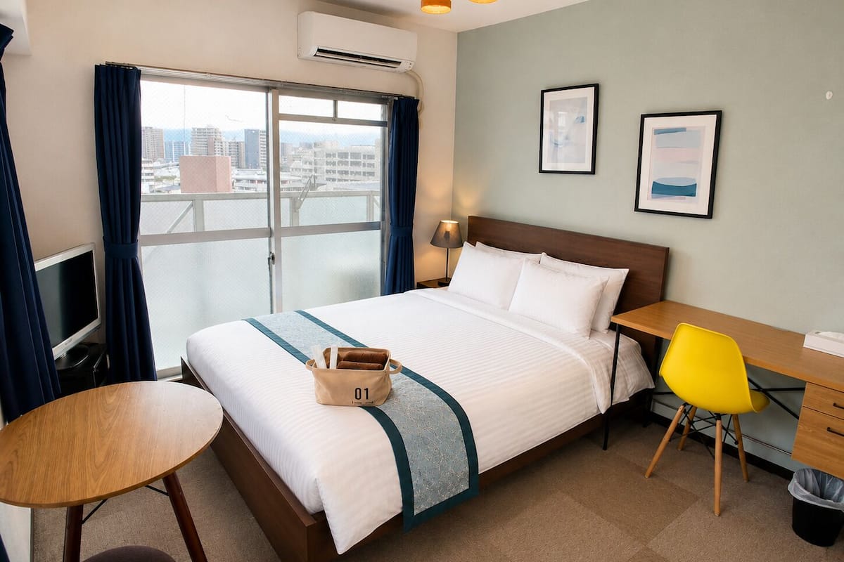 Una habitación de hotel con cama, escritorio, silla, televisión y ventana con cortinas.