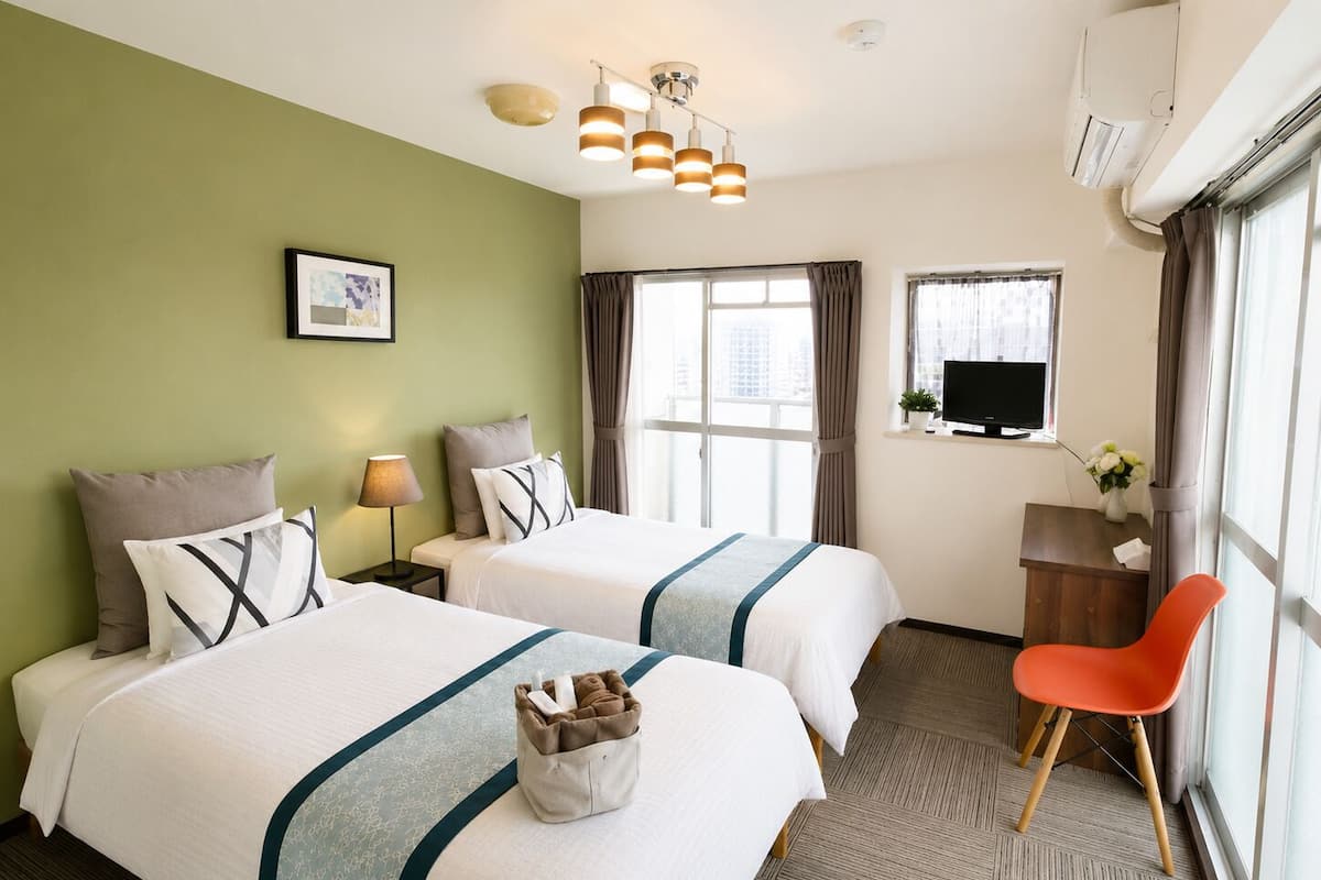 Habitación de hotel con dos camas, un escritorio, una silla, un televisor y una ventana con cortinas.